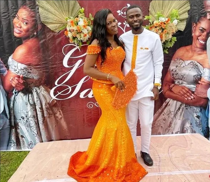 A couple at their reception; the bride carries a beaded orange clutch matched to her dress.